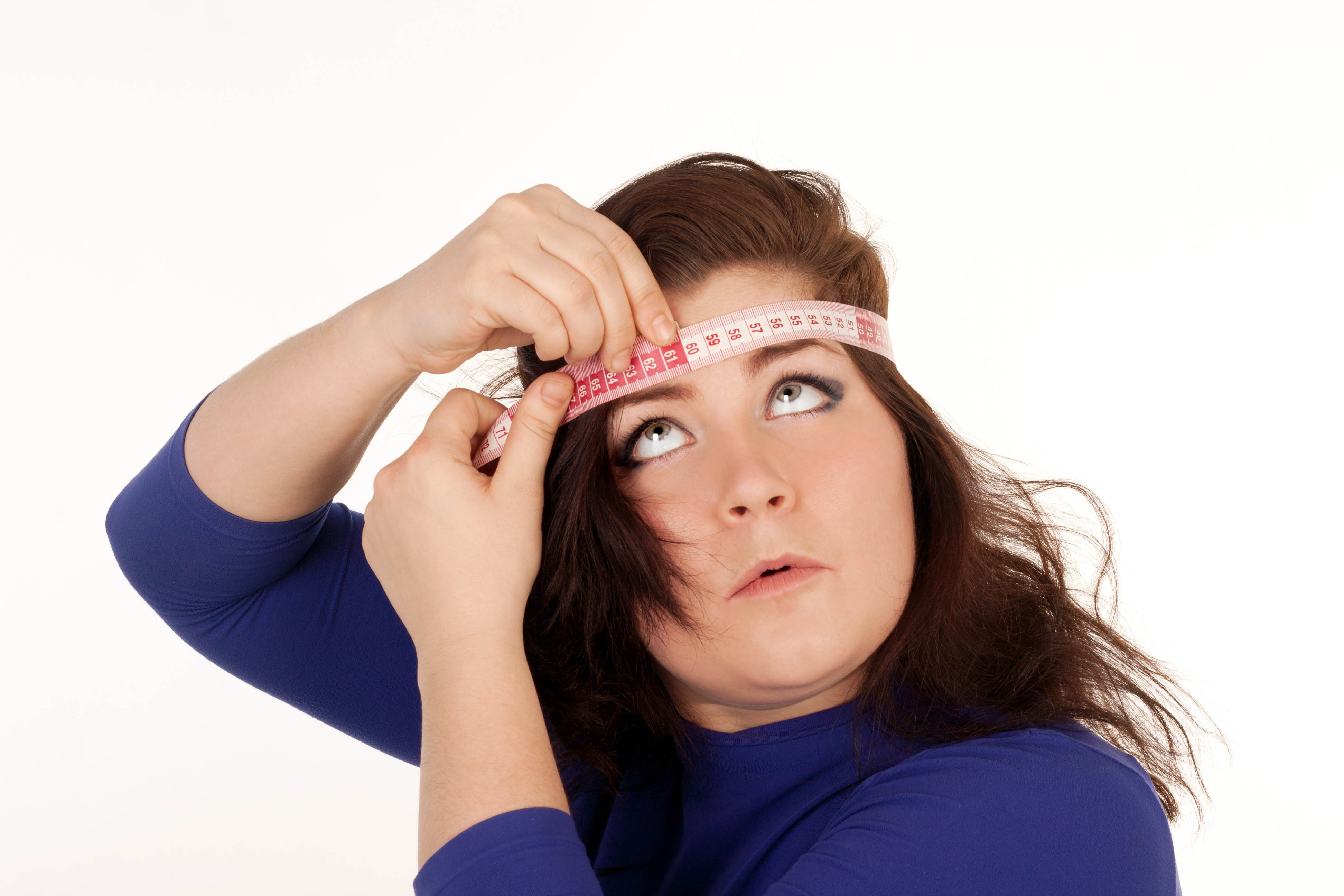 Bigger, young woman wrapping a tape measure around her head to measure her head